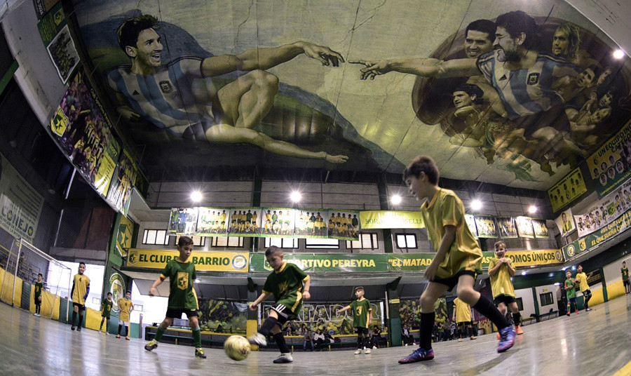 Kids play indoor soccer at the Sportivo Pereyra de Barracas club in Buenos Aires, which features Lionel Messi and Diego Maradona painted into a unique version of Michelangelo's 'Creation of Adam' on the ceiling. [Photo/Agencies]